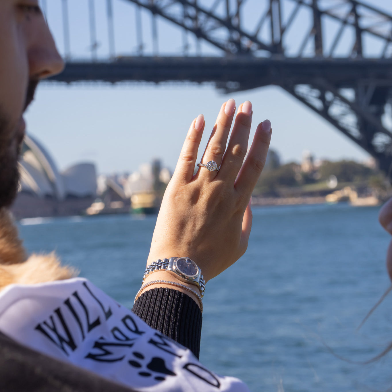 Person holding hand with ring near Sydney Harbour Bridge
